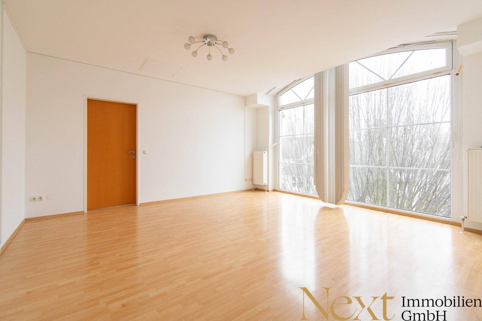Geräumiges Wohnzimmer mit hellem Parkettboden und großen, bogenförmigen Fenstern für viel Tageslicht.