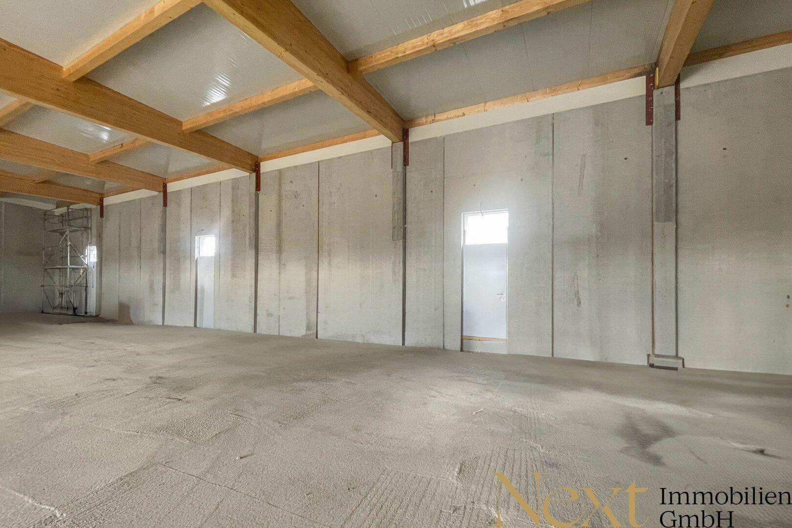 Innenansicht einer modernen Lagerhalle mit hohen Betonwänden und Holzdachkonstruktion.