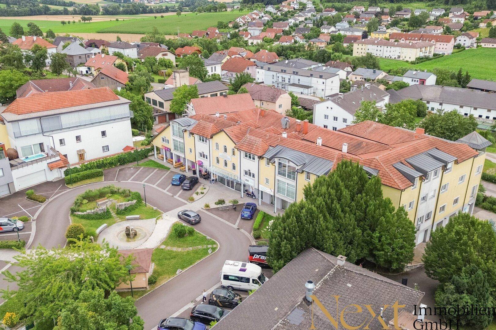 Weitläufige Luftaufnahme eines Wohngebiets mit mehreren Gebäuden, Parkplätzen und ländlicher Umgebung.