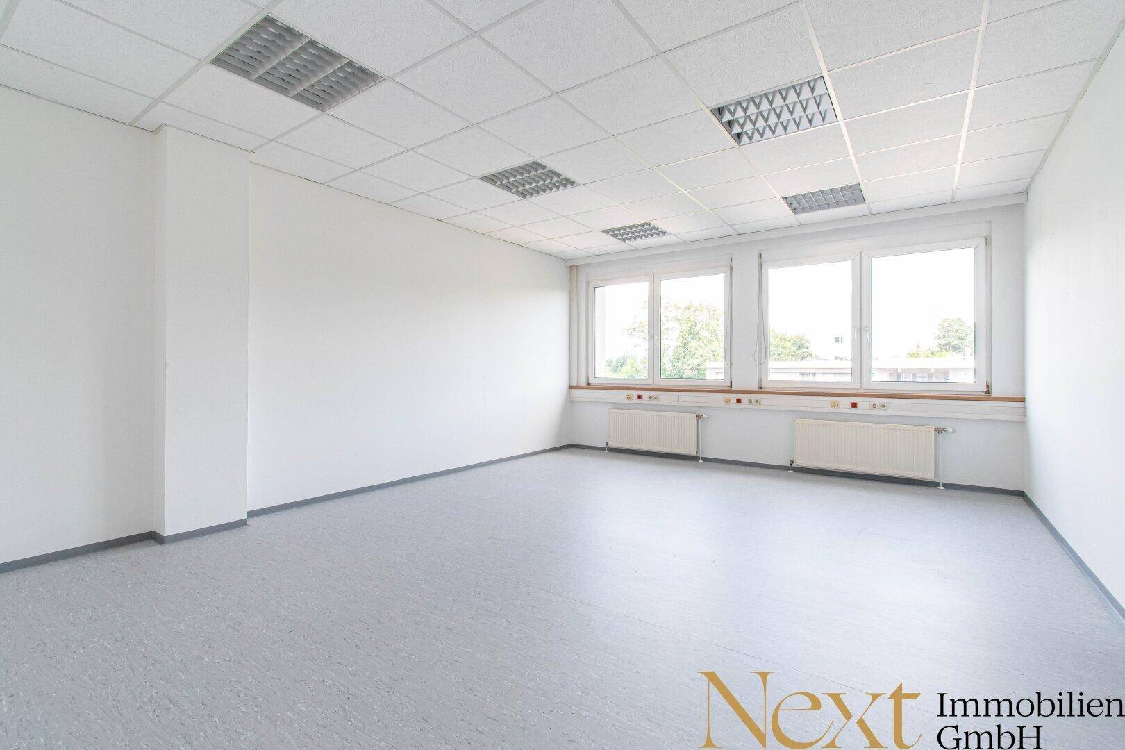 Helles Büro mit grauem Vinylboden, weißen Wänden und großen Fenstern, die viel Tageslicht hereinlassen.