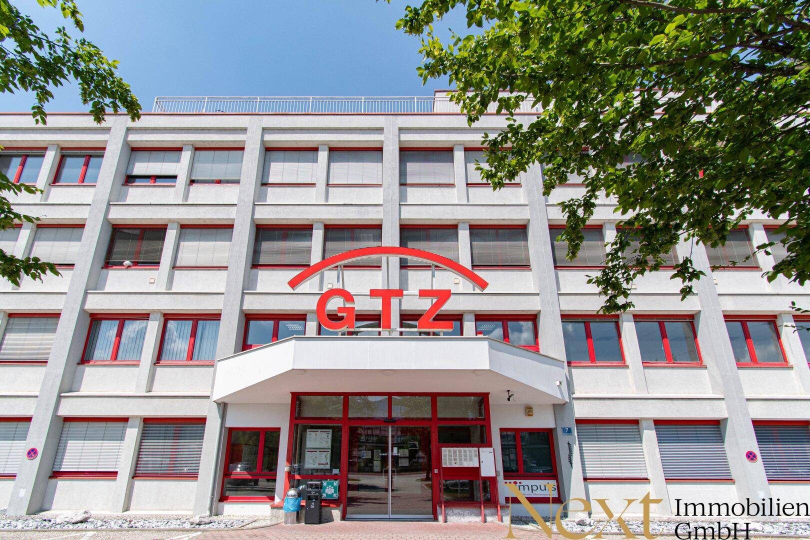 Vorderansicht des modernen Bürogebäudes mit markantem Eingangsbereich und roten Fensterrahmen.