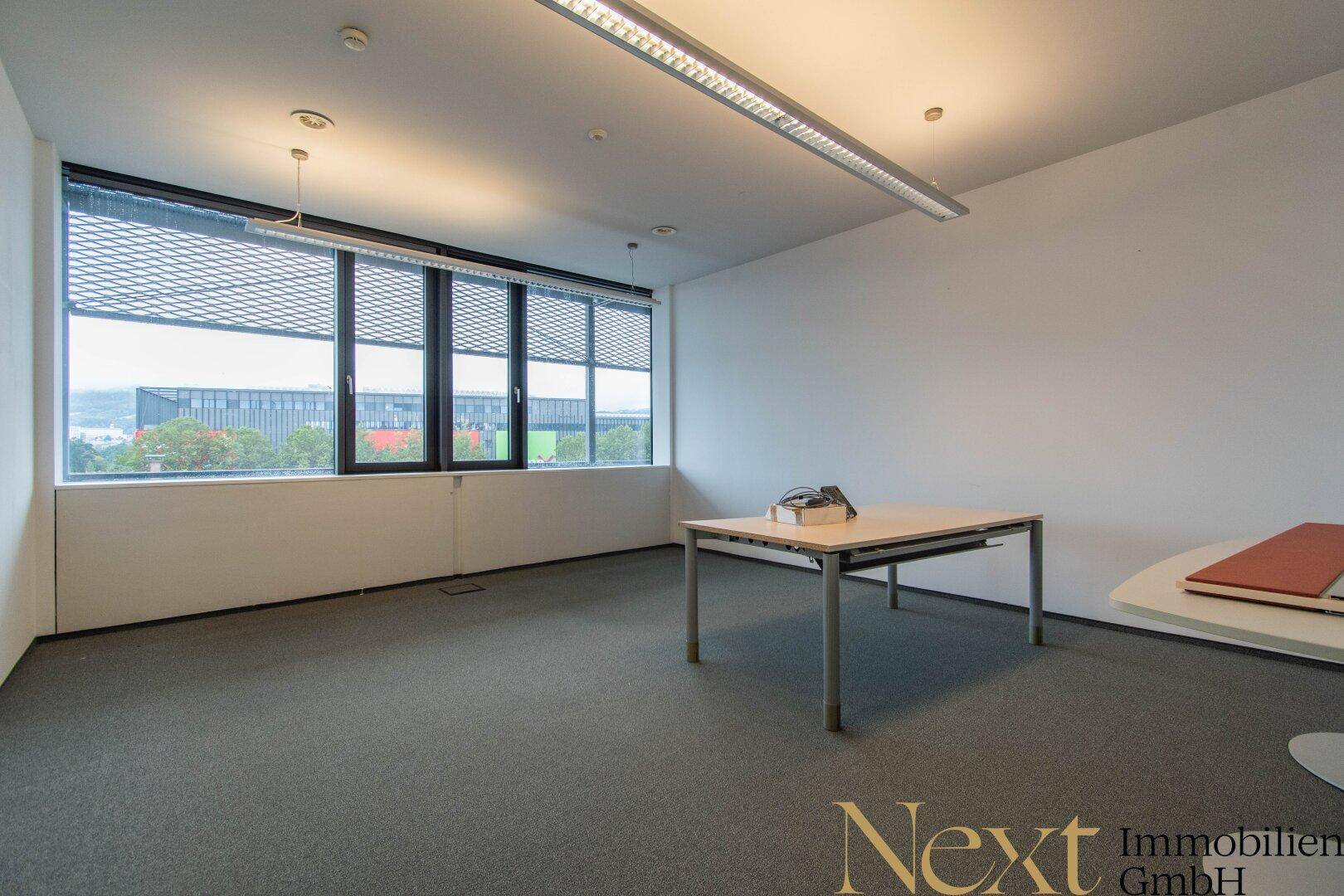 Geräumiges Büro mit Teppichboden, großen Fenstern und weitem Blick auf die Umgebung.