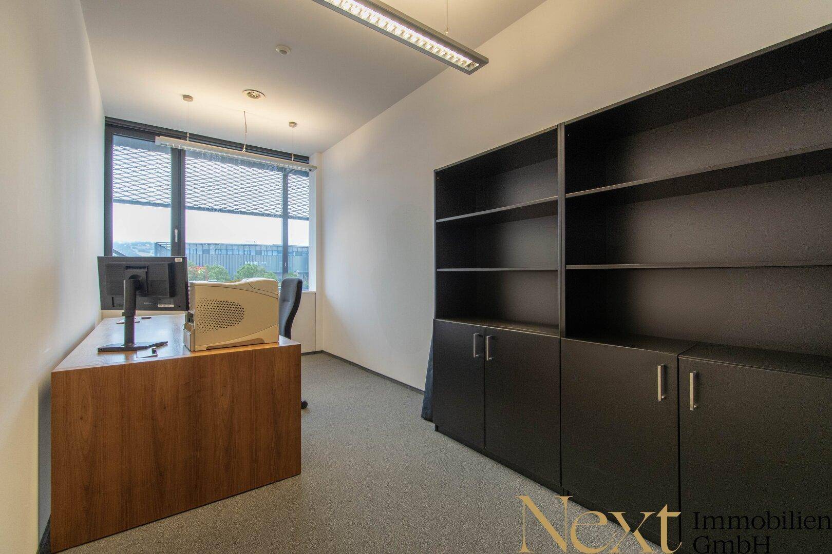 Funktionales Büro mit Schreibtisch, Computer und dunklen Regalschränken, gut beleuchtet.