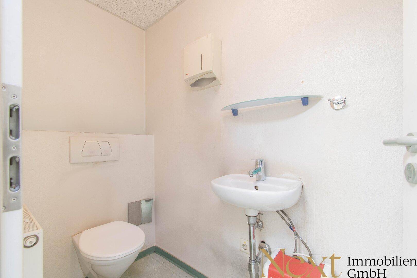 Kleines, einfaches WC mit wandhängender Toilette und Handwaschbecken, funktional und sauber.