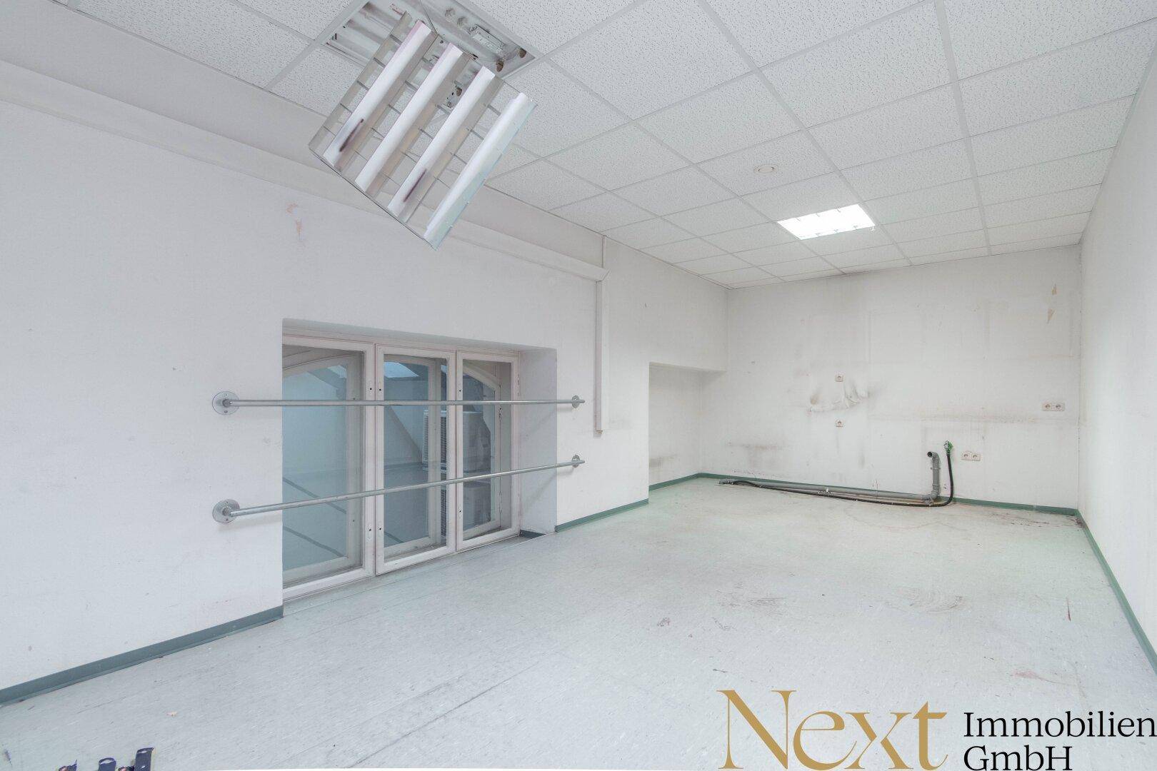 Großer, leerer Gewerberaum mit Fensterfront und abgehängter Decke, bietet vielseitige Nutzungsmöglichkeiten.