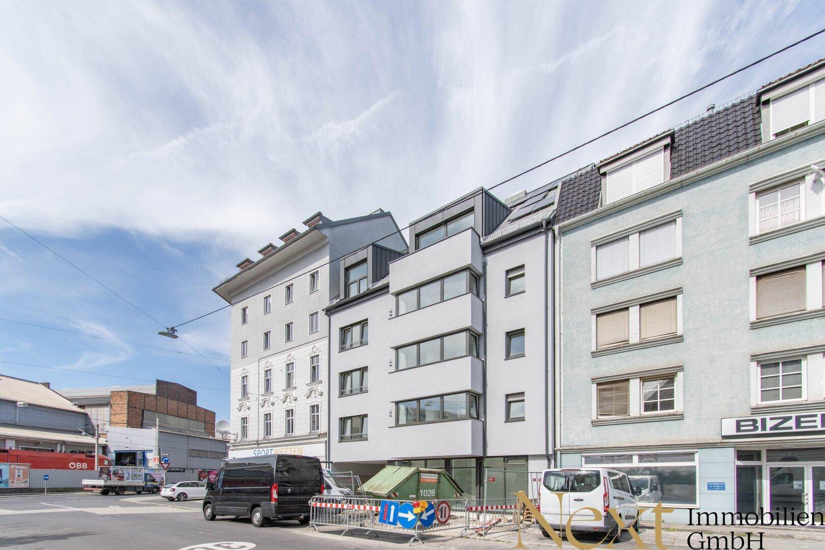 Moderne Gebäudefassade an einer städtischen Straße mit angrenzenden Altbauten.