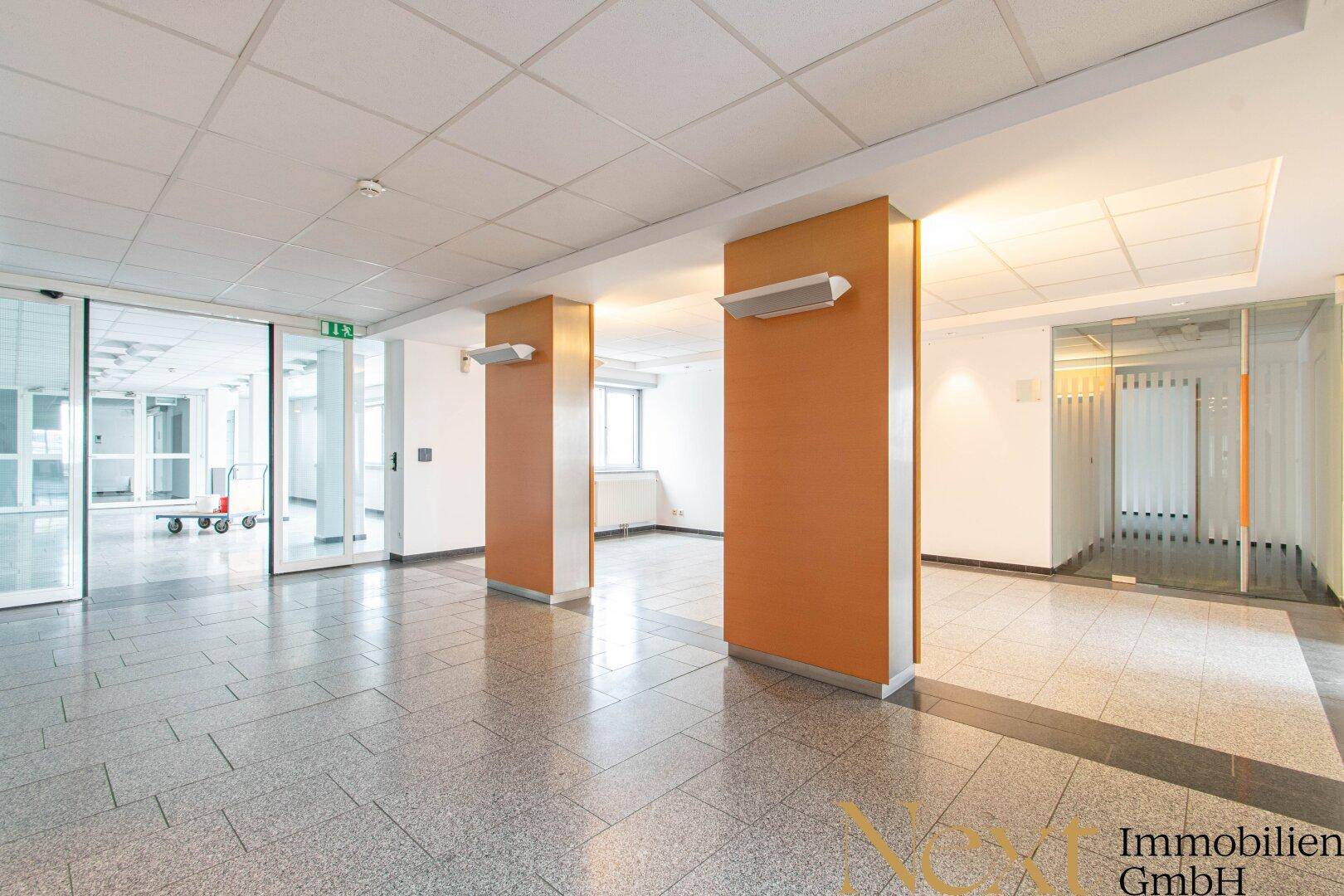 Offener Bereich mit Fliesenboden, Säulen und Glasschiebetüren, die zu weiteren Räumen führen.