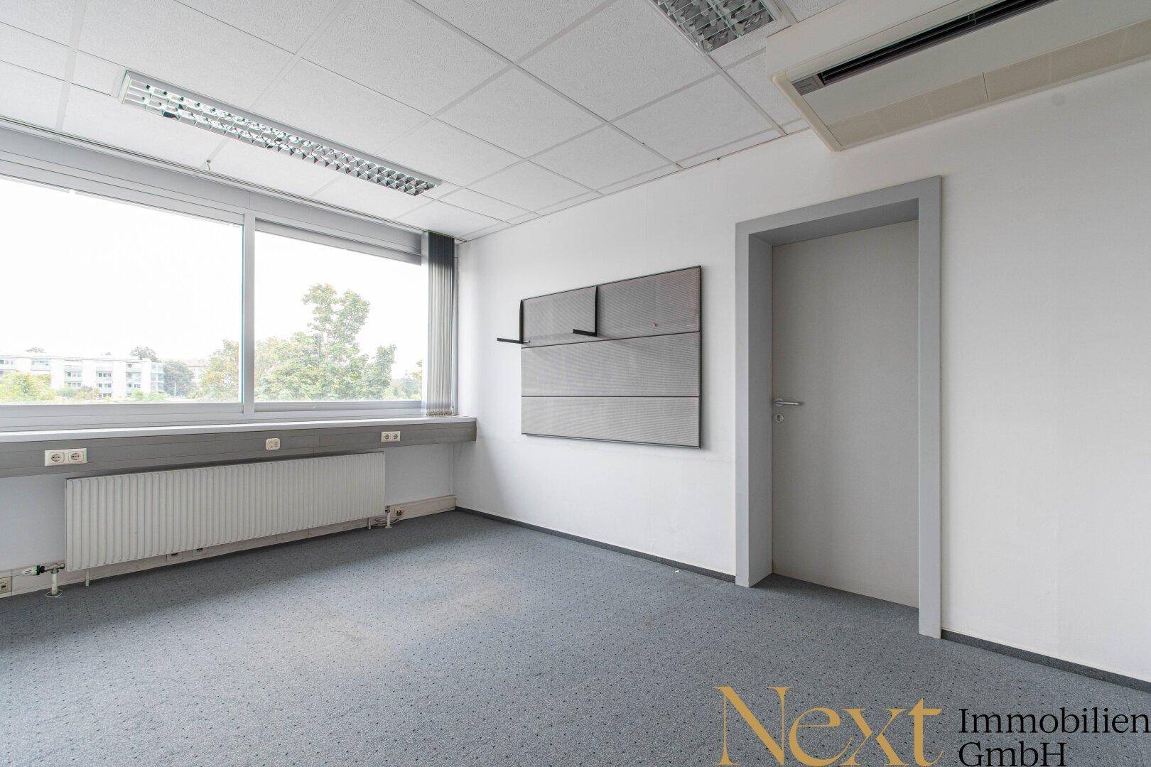 Einzelbüro mit grauem Teppichboden, großem Fenster und Heizkörper unter der Fensterbank.
