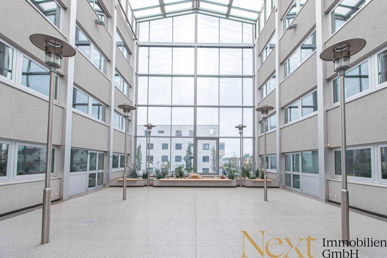 Helles Atrium mit Glasdach und großen Fenstern, das viel Tageslicht in den Innenbereich bringt.