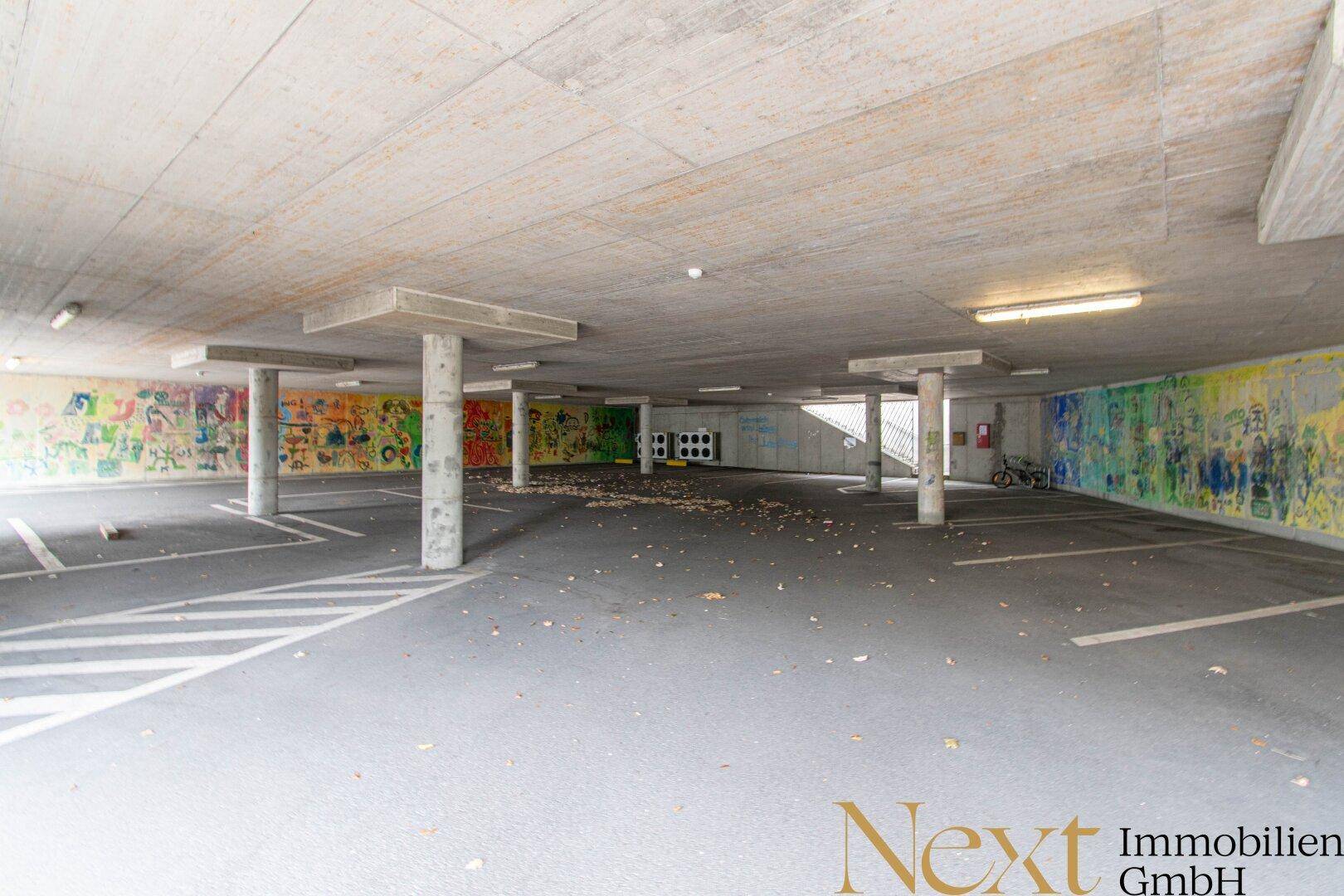 Tiefgarage mit Betonpfeilern und bunten Graffiti an den Wänden, bietet viele Stellplätze.