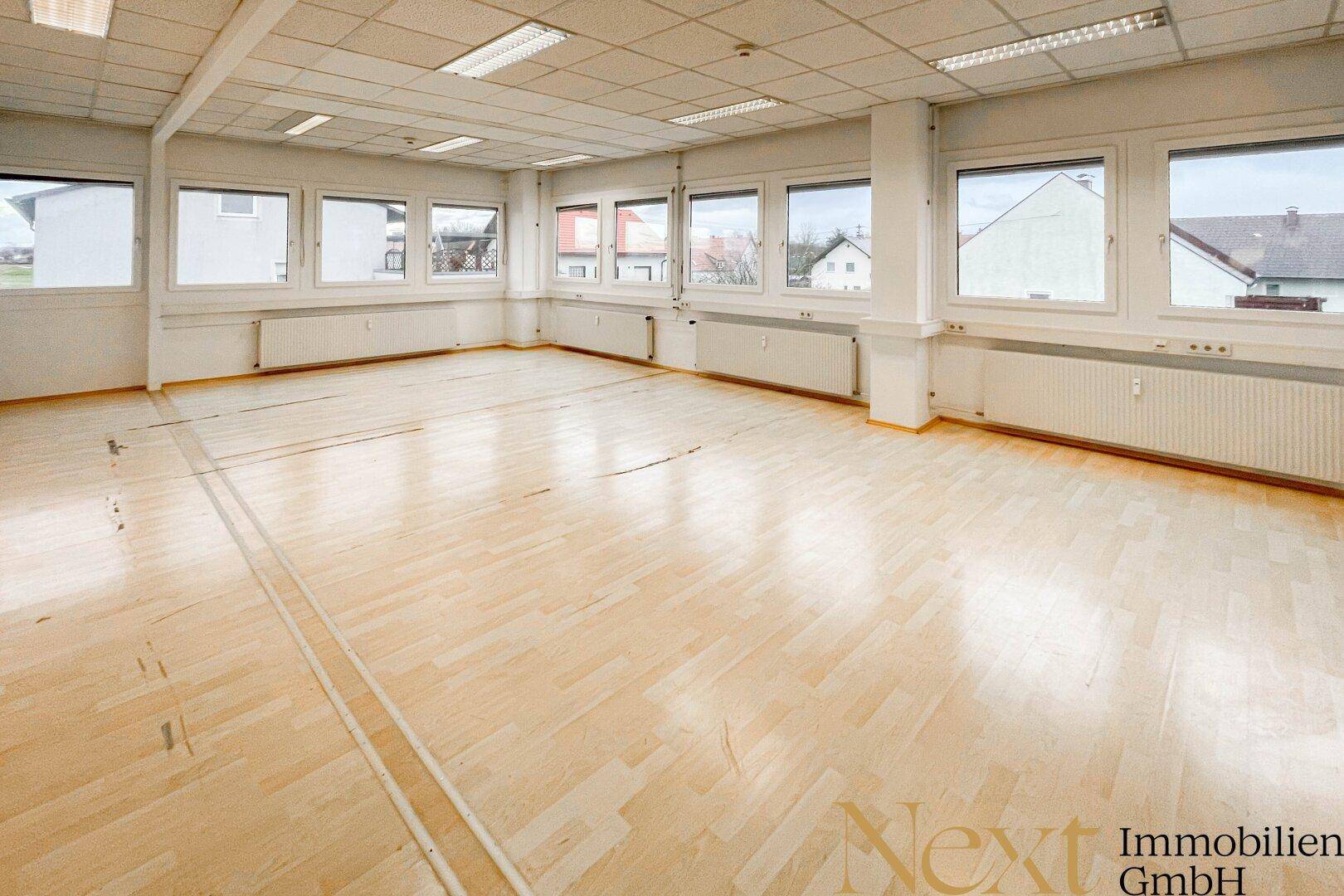 Helles, leeres Büro mit hellem Laminatboden und vielen Fenstern, die einen Blick auf die Nachbarschaft bieten.