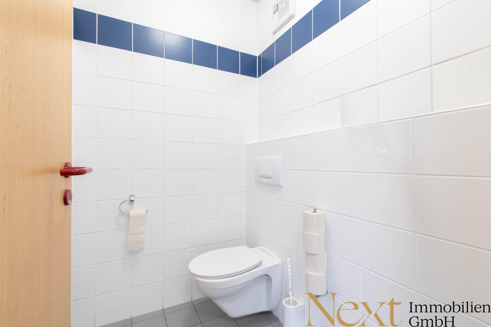 Saubere Toilette mit weißen Fliesen und einem blauen Akzentstreifen, ausgestattet mit Wand-WC.