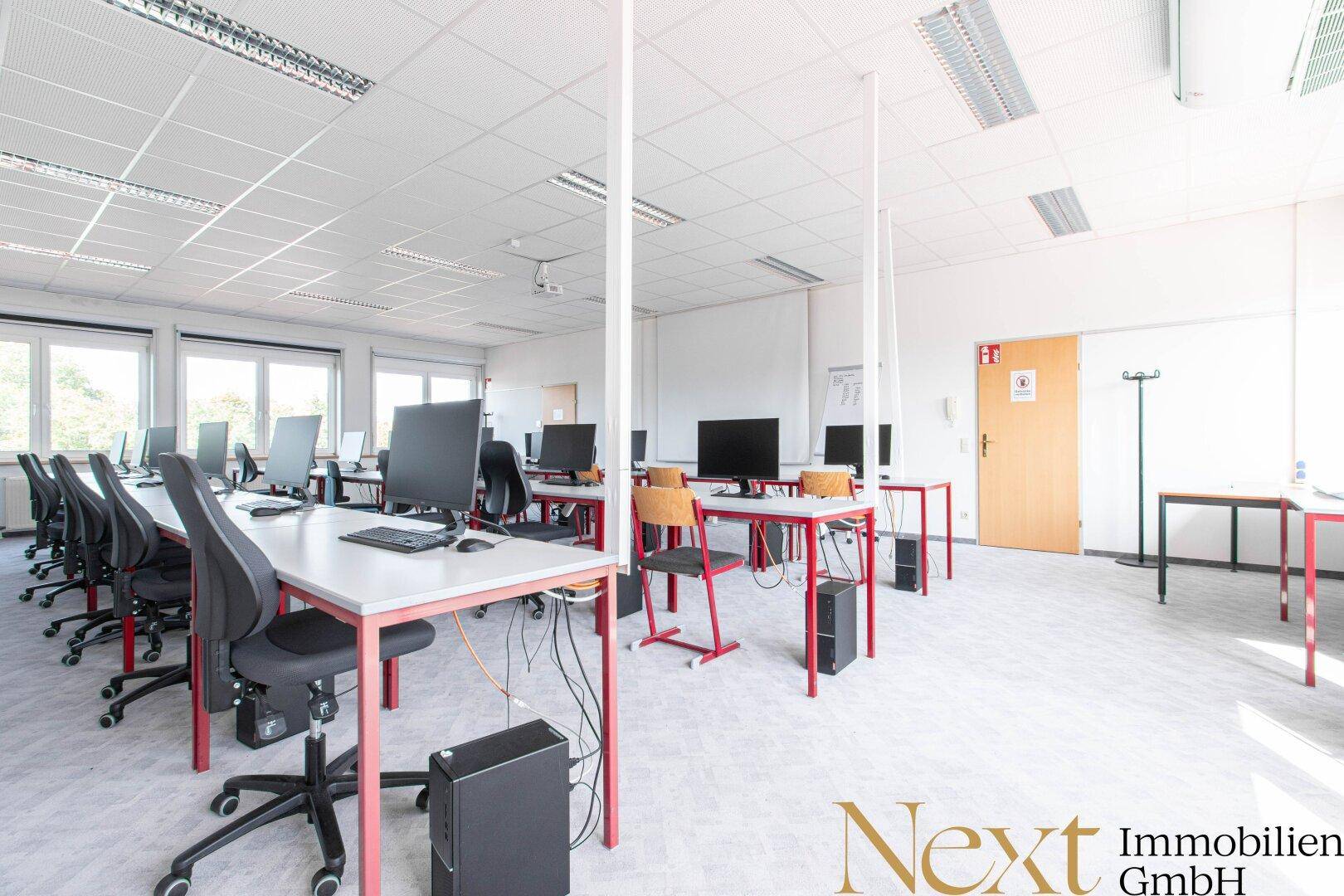 Geräumiger Computerraum mit mehreren Arbeitsplätzen, Monitoren und ergonomischen Bürostühlen.
