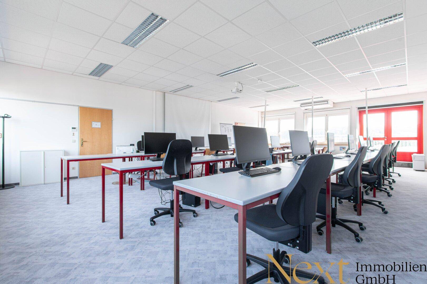 Moderner Schulungsraum mit Reihen von Computertischen und Bürostühlen, ideal für Bildungszwecke.