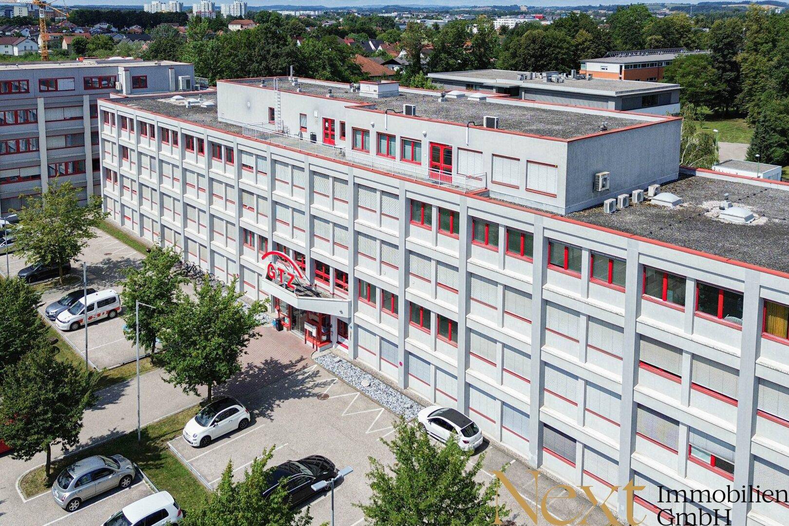 Luftaufnahme eines großen Bürogebäudes mit vielen Fenstern, Parkplätzen und umliegender Grünfläche.