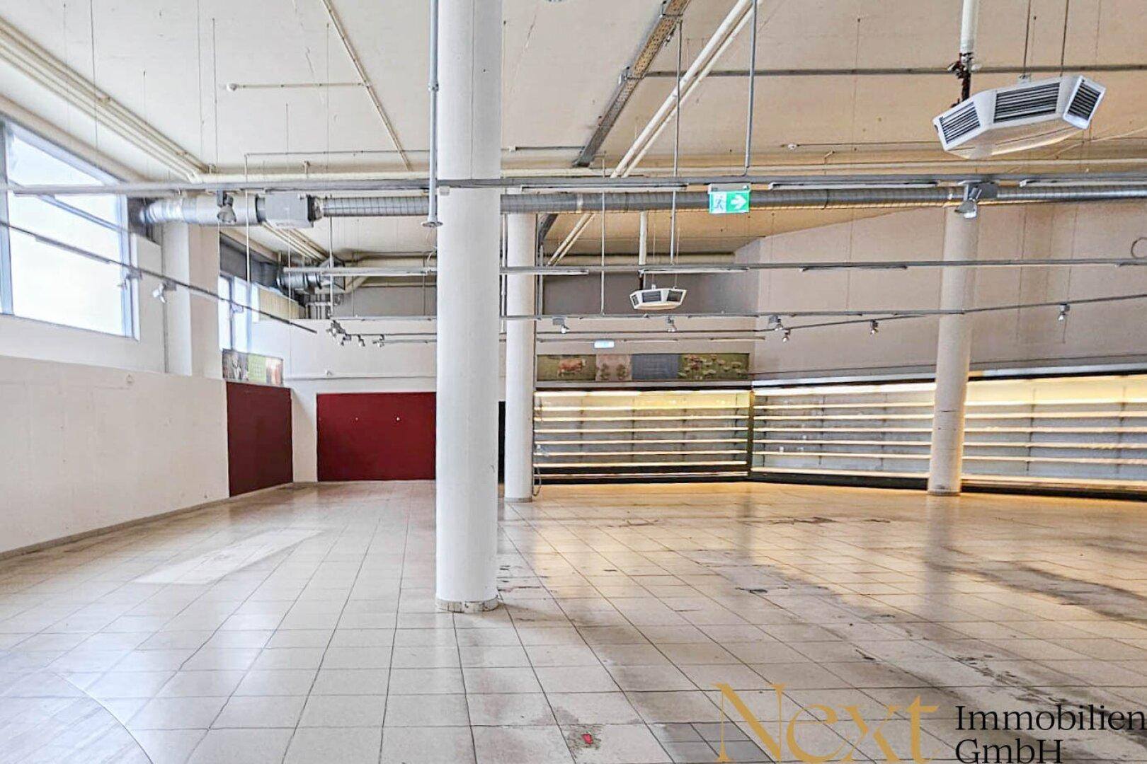 Geräumiger, leerer Verkaufsraum mit Säulen, Fliesenboden und großen Fenstern, ideal für Einzelhandel.