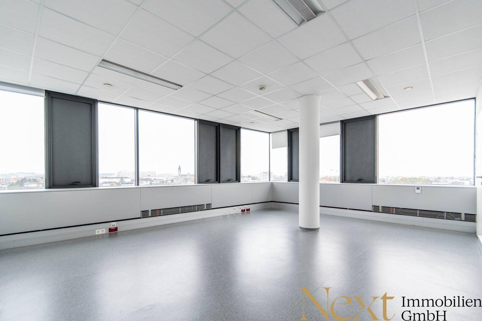 Moderner Büroraum mit glattem Boden, vielen Fenstern und einer zentralen Säule, bietet flexible Nutzungsmöglichkeiten.