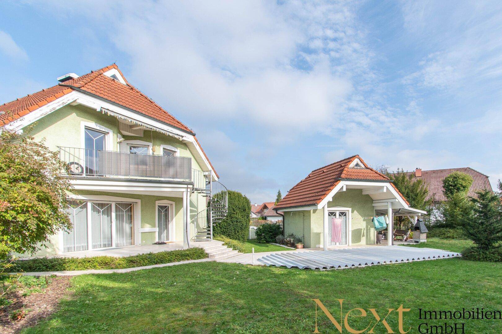 Ansicht des Hauses und eines Nebengebäudes mit großem, gepflegtem Rasen und Terrasse.