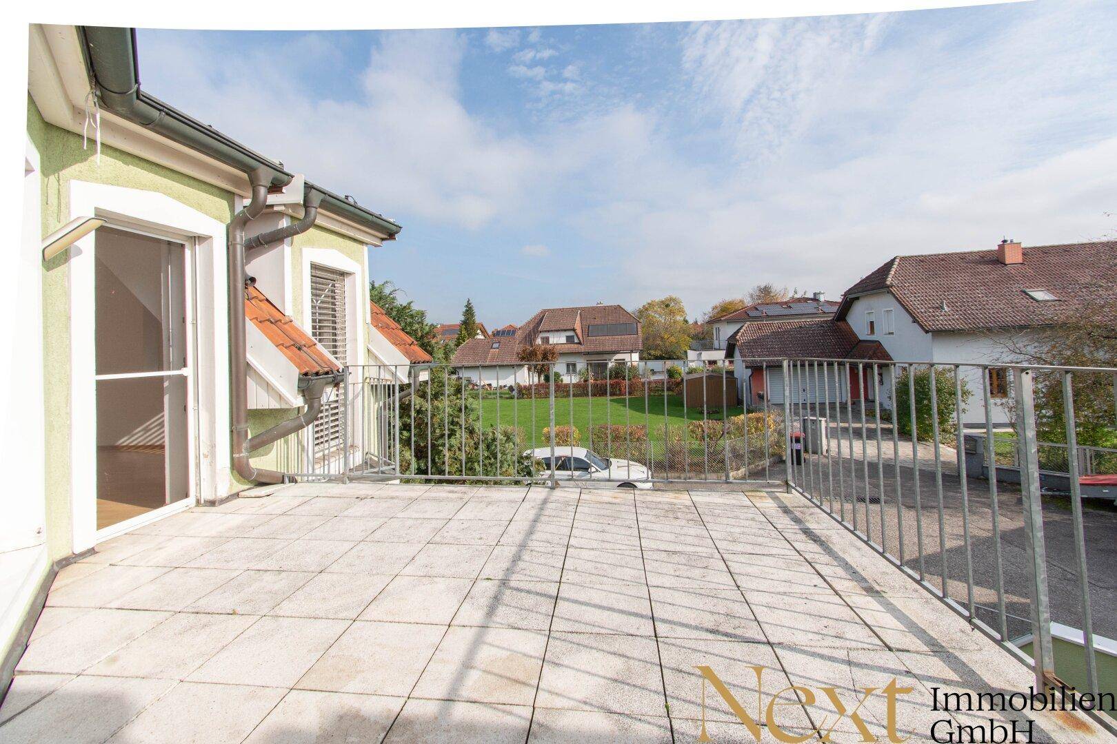 Geräumige geflieste Terrasse mit Metallgeländer und Blick auf die umliegenden Häuser und Gärten.
