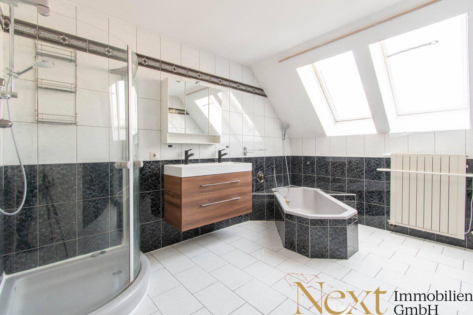 Badezimmer im Dachgeschoss mit Eckbadewanne, Duschkabine und zwei Dachfenstern.