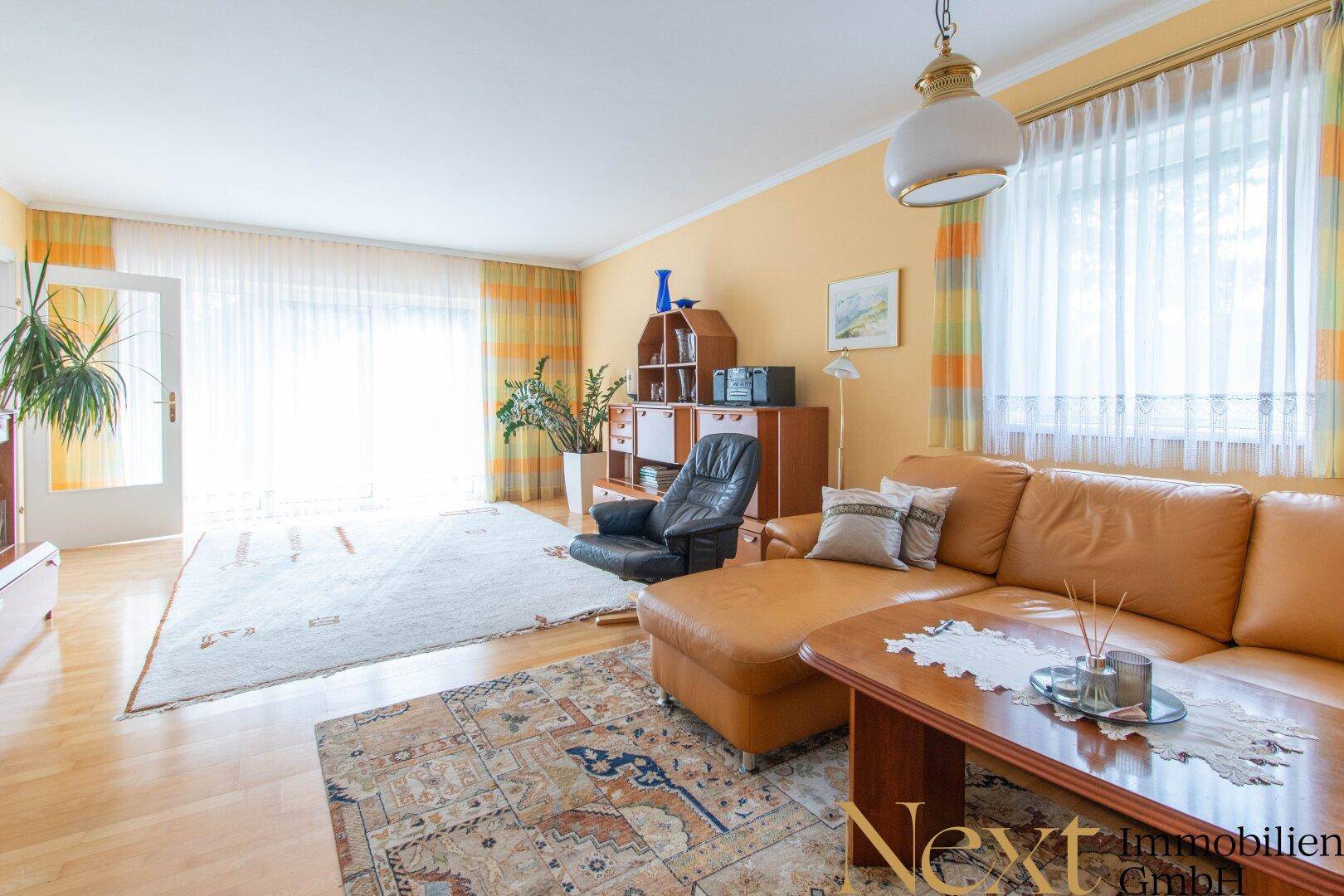 Gemütliches Wohnzimmer mit Ledersofa, Parkettboden und großen Fenstern für viel Tageslicht.