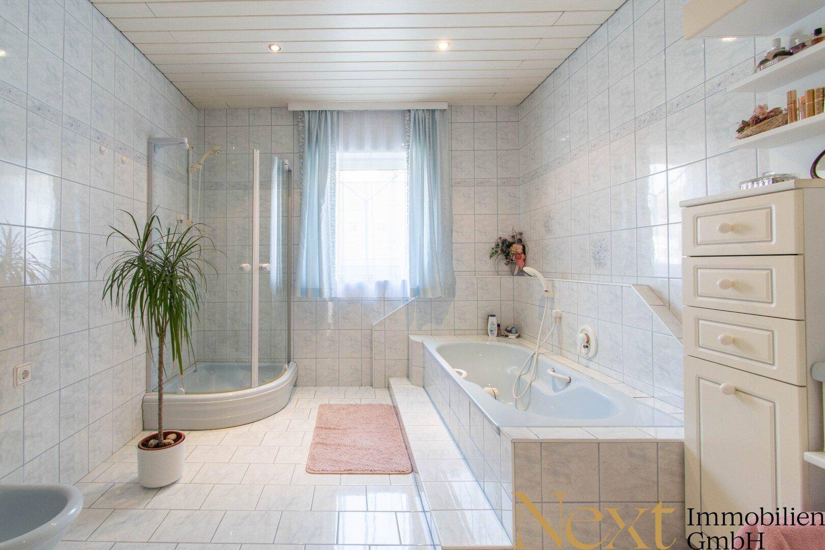 Helles Badezimmer mit Badewanne, Duschkabine, Fenster und weißen Fliesen.