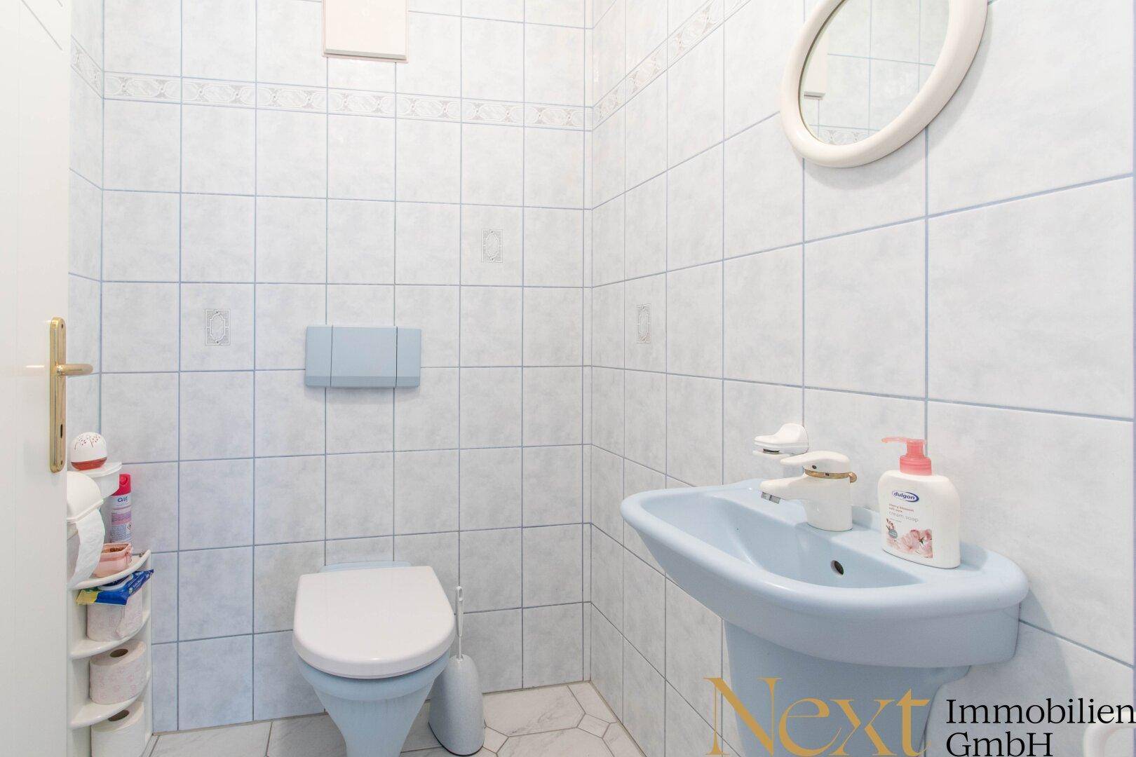 Kleines Gäste-WC mit hellblauen Fliesen, Toilette und Waschbecken.