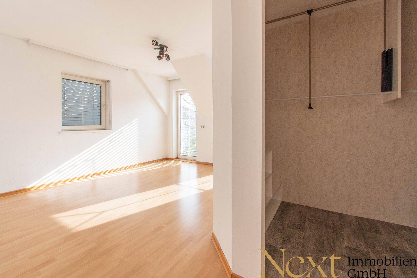 Heller Raum mit Holzfußboden, einem Fenster und einem angrenzenden Bereich, möglicherweise für einen Einbauschrank.