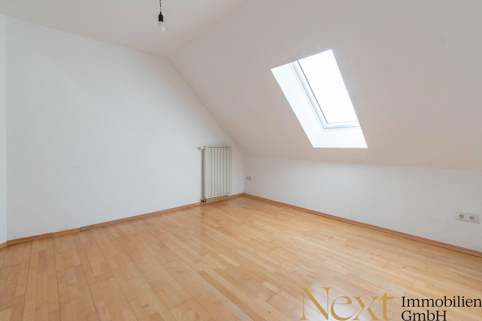 Dachgeschosszimmer mit schrägen Wänden, Holzfußboden und einem Dachfenster für natürliches Licht.