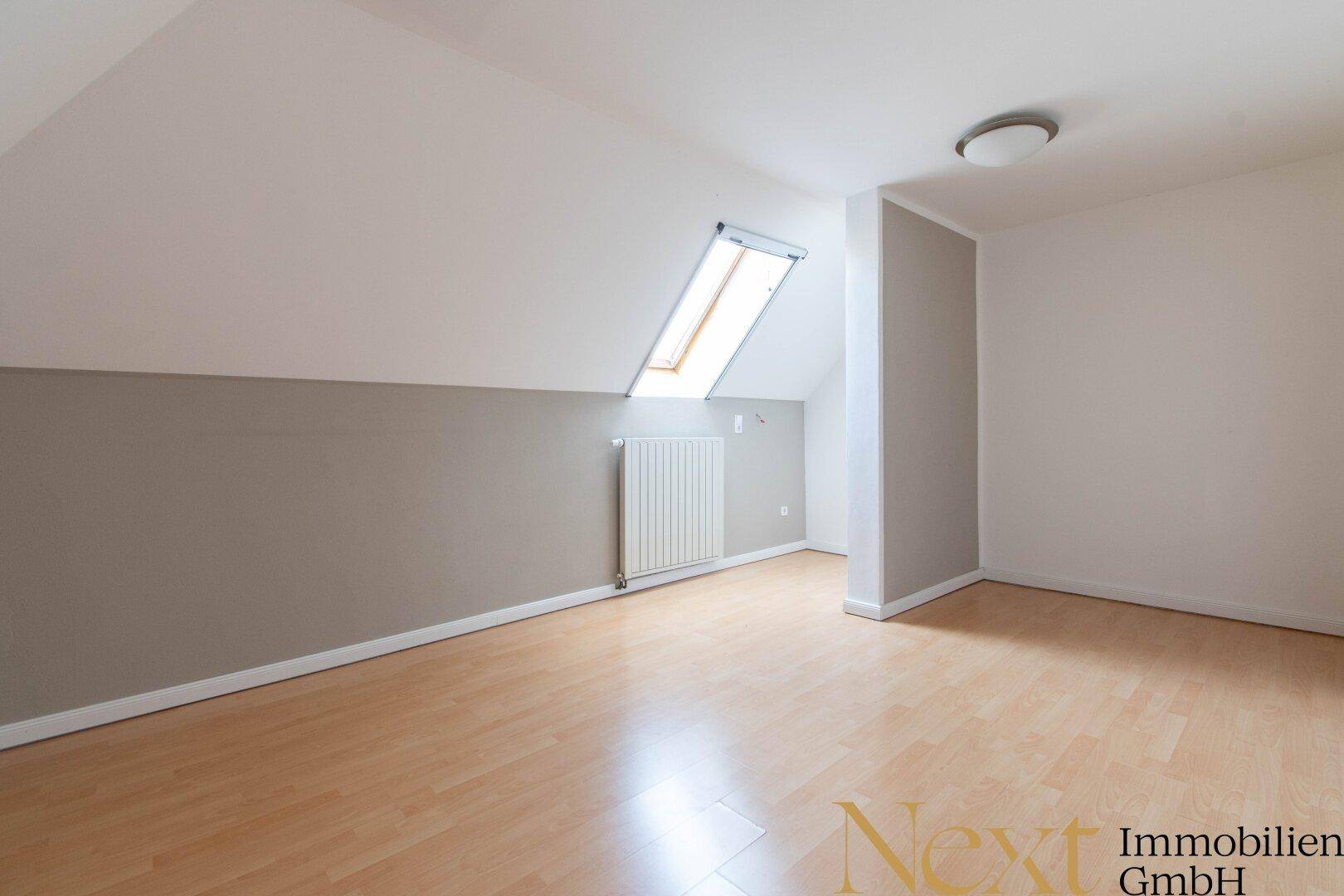 Helles Dachgeschosszimmer mit Holzfußboden, Dachfenster und einer zweifarbigen Wandgestaltung.