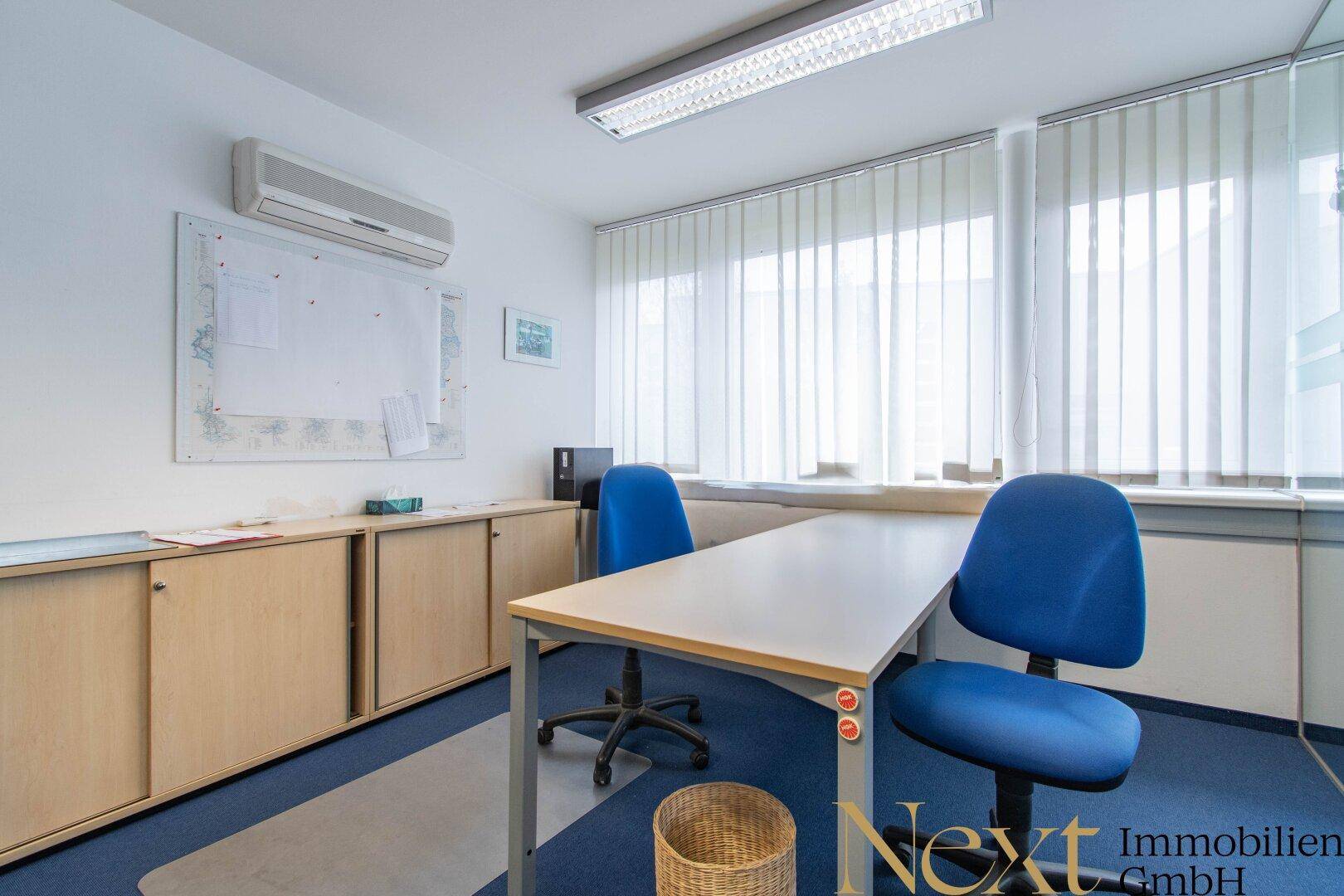 Modernes Büro mit Klimaanlage, Schreibtisch und blauen Bürostühlen, ergänzt durch praktische Einbauschränke.