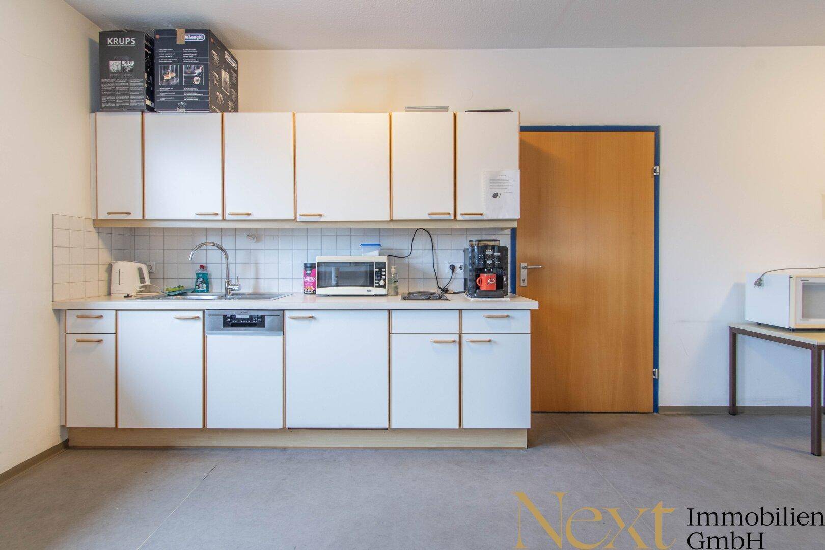 Funktionale Küchenzeile mit weißen Schränken, Spülmaschine und Mikrowelle, ideal für die Zubereitung kleiner Mahlzeiten.