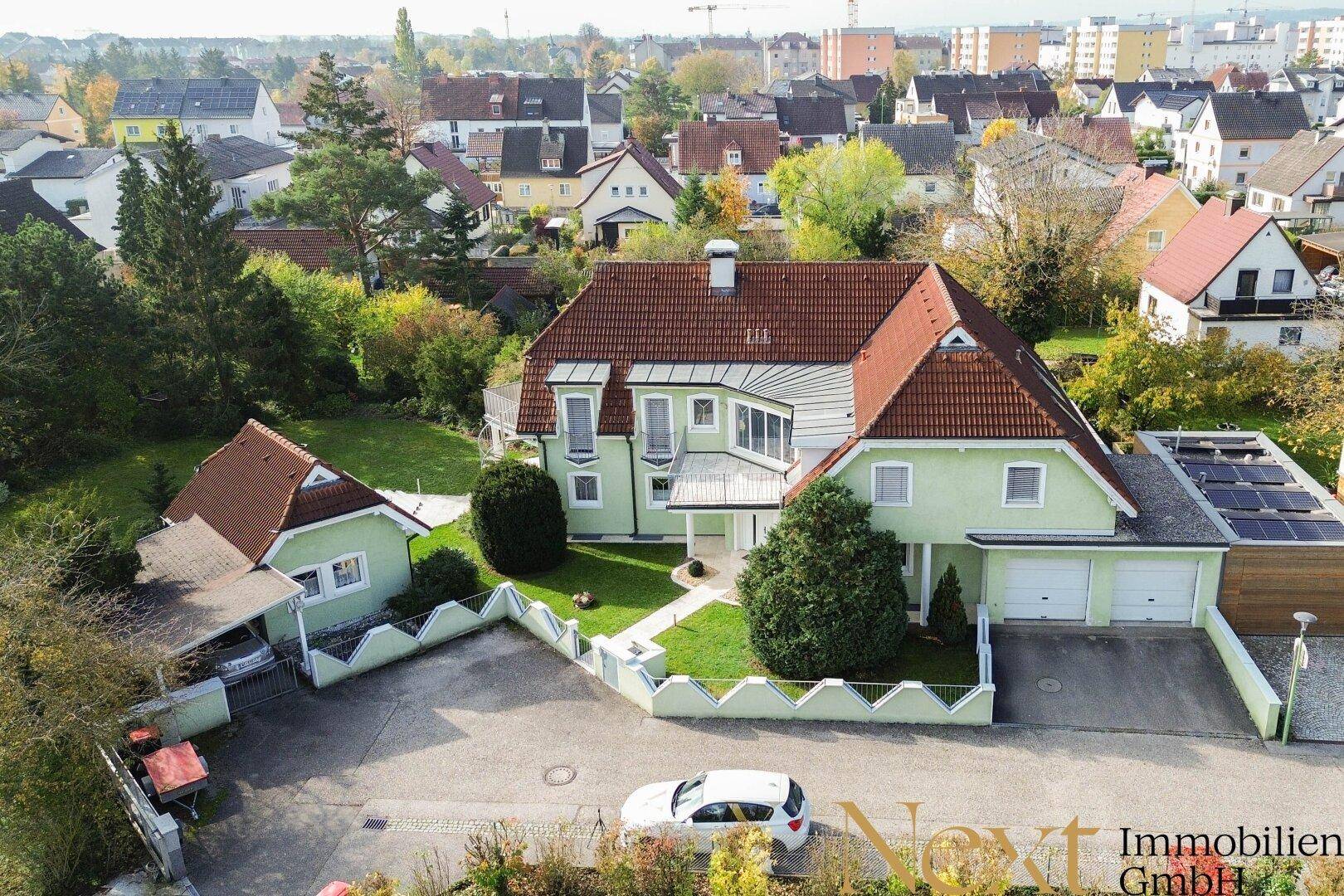 Luftaufnahme eines Einfamilienhauses mit rotem Ziegeldach, grüner Fassade und Doppelgarage.