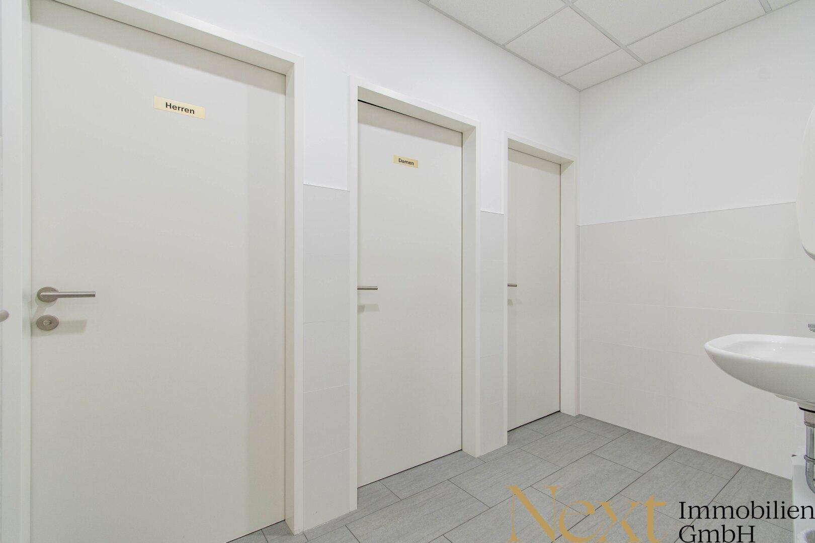 Flur mit Zugang zu mehreren Toiletten, ausgestattet mit einem Waschbecken und modernem Fliesenboden.