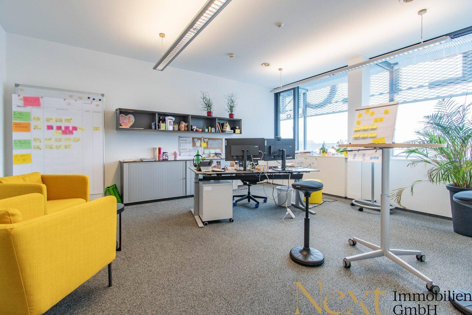 Geräumiges Büro mit mehreren Arbeitsbereichen, bequemen gelben Sesseln und modernen Büromöbeln.