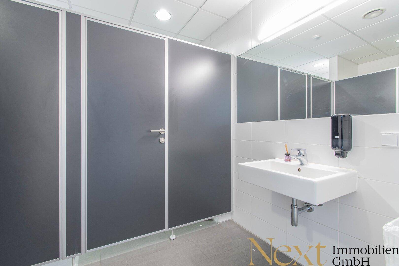 Moderne Toilettenkabinen in einem Waschraum mit Waschbecken und großem Spiegel.