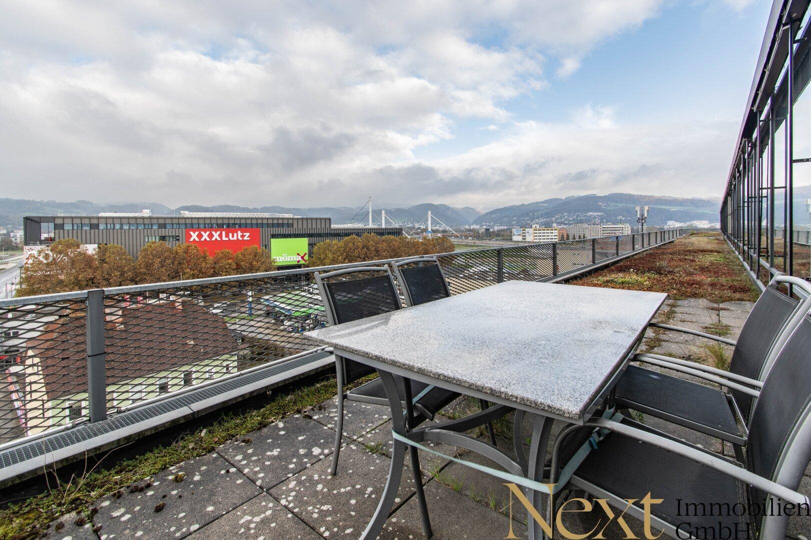 Dachterrasse mit Steinfliesen, einem Tisch und Stühlen, bietet einen weiten Blick über die Stadt.