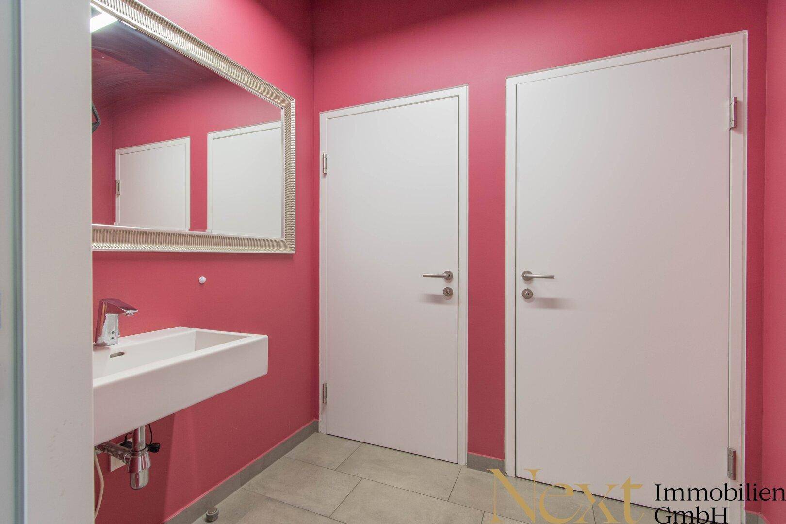 Modernes Damenbad mit leuchtend rosa Wänden, einem stilvollen Waschbecken und zwei weißen Türen.