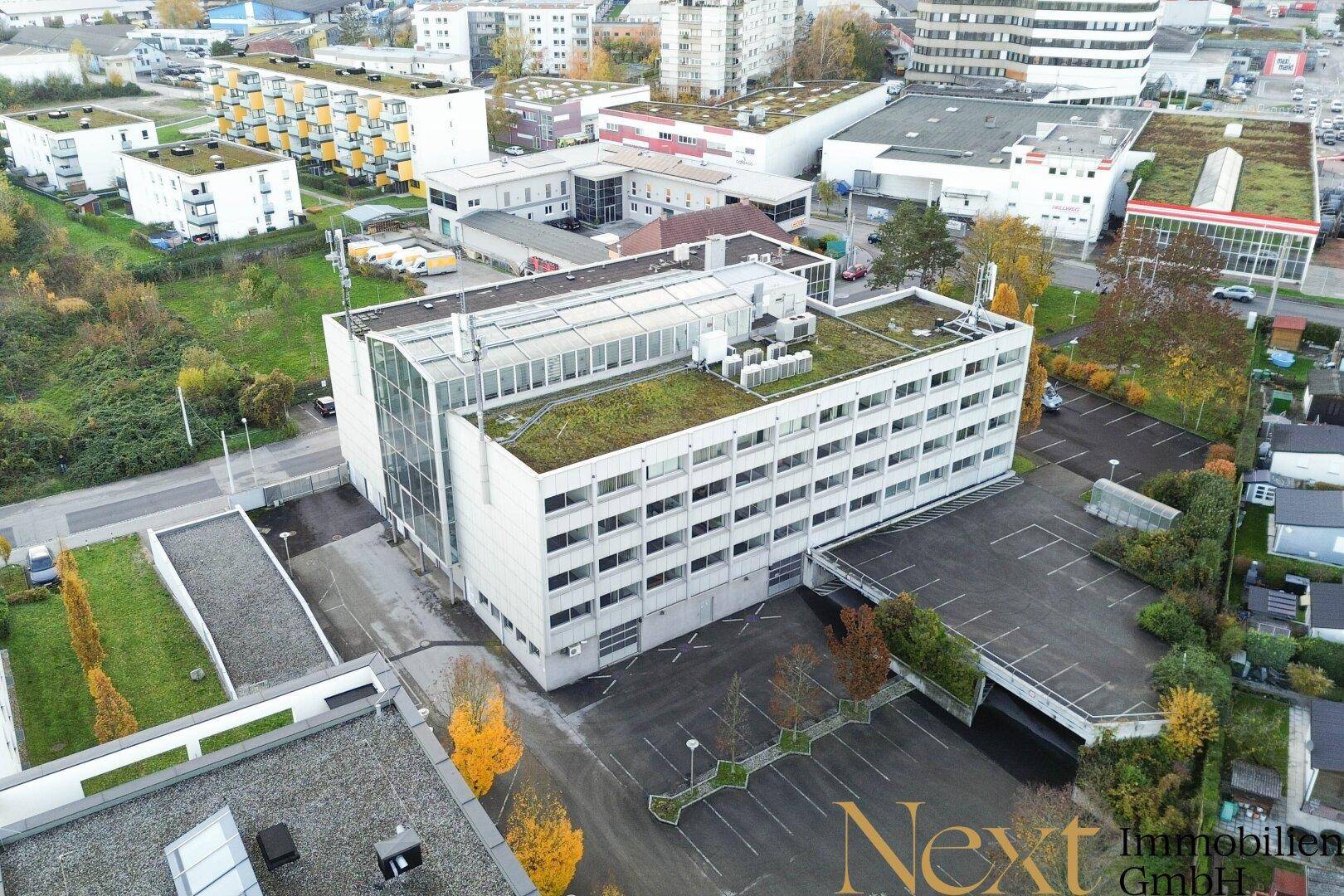 Weitere Luftaufnahme des Gebäudekomplexes mit umliegenden Grünflächen und Parkplätzen.