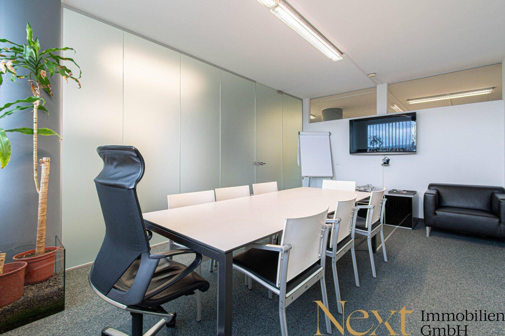 Moderner Konferenzraum mit großem Besprechungstisch, Medientechnik und bequemen Stühlen für produktive Meetings.