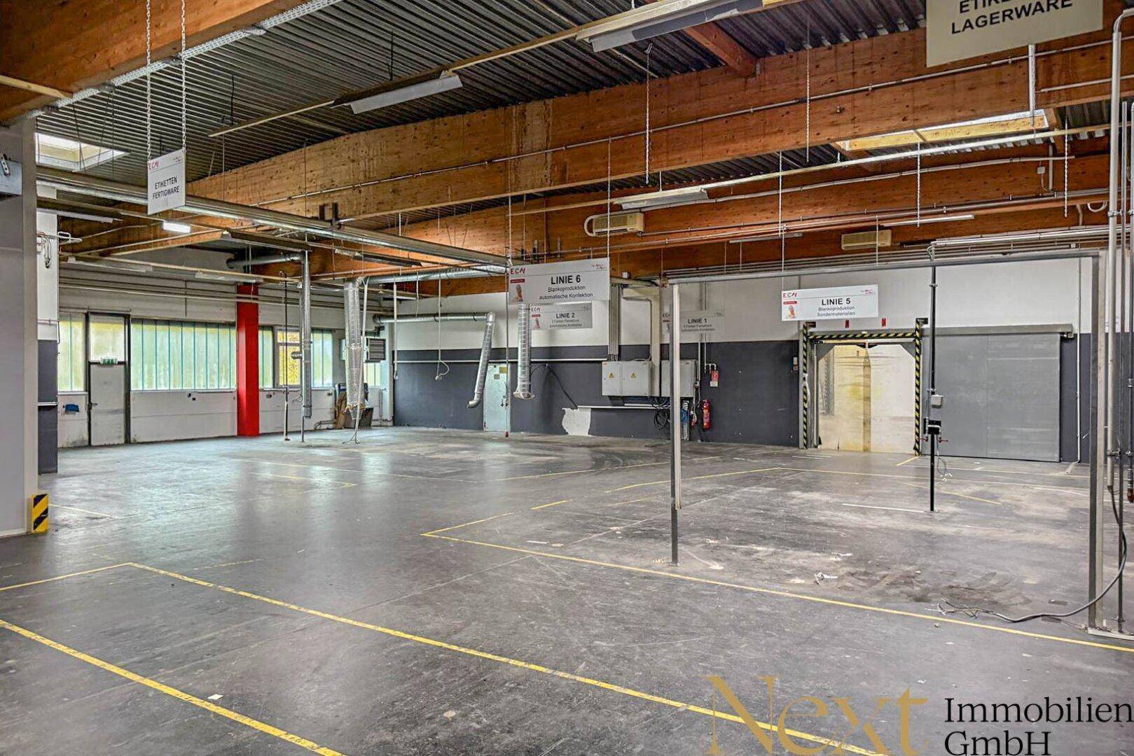 Weitläufige Lagerhalle mit sichtbaren Holzbalken, Metallkonstruktion und industriellem Betonboden.