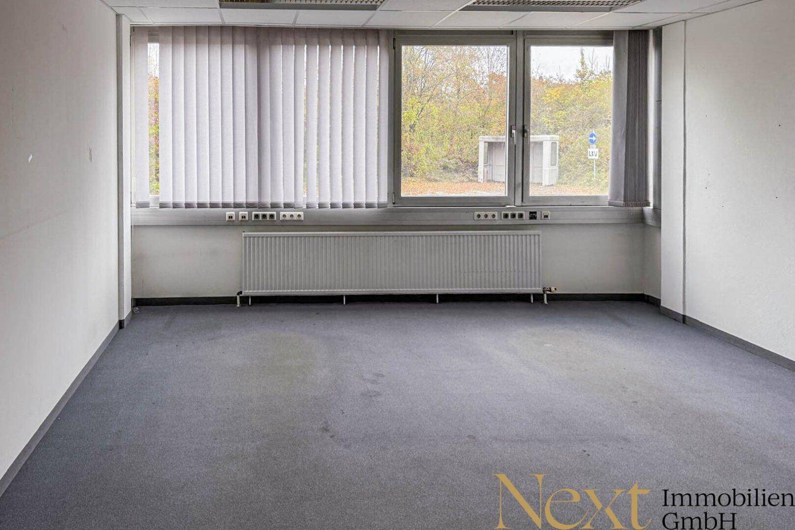 Helles Büro mit Teppichboden, großen Fenstern und Heizkörpern unter den Fensterbänken.