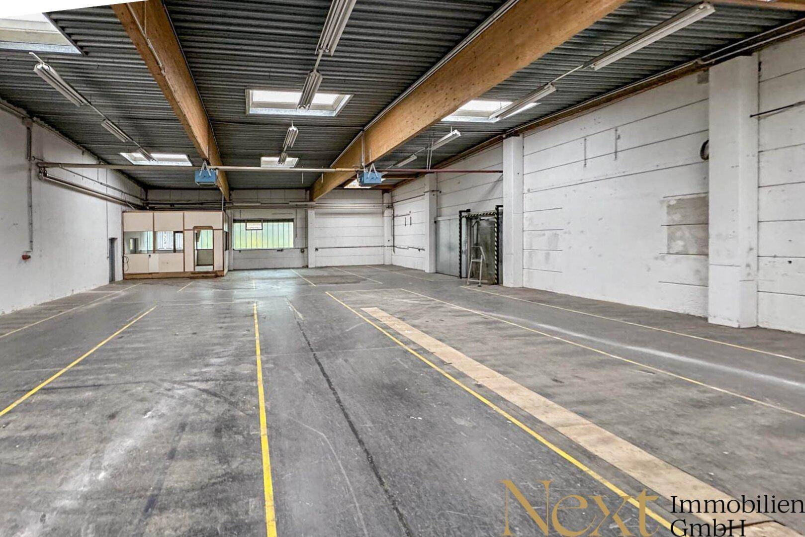 Geräumige Lagerhalle mit hohen Decken, Oberlichtern und Betonboden mit Markierungen.