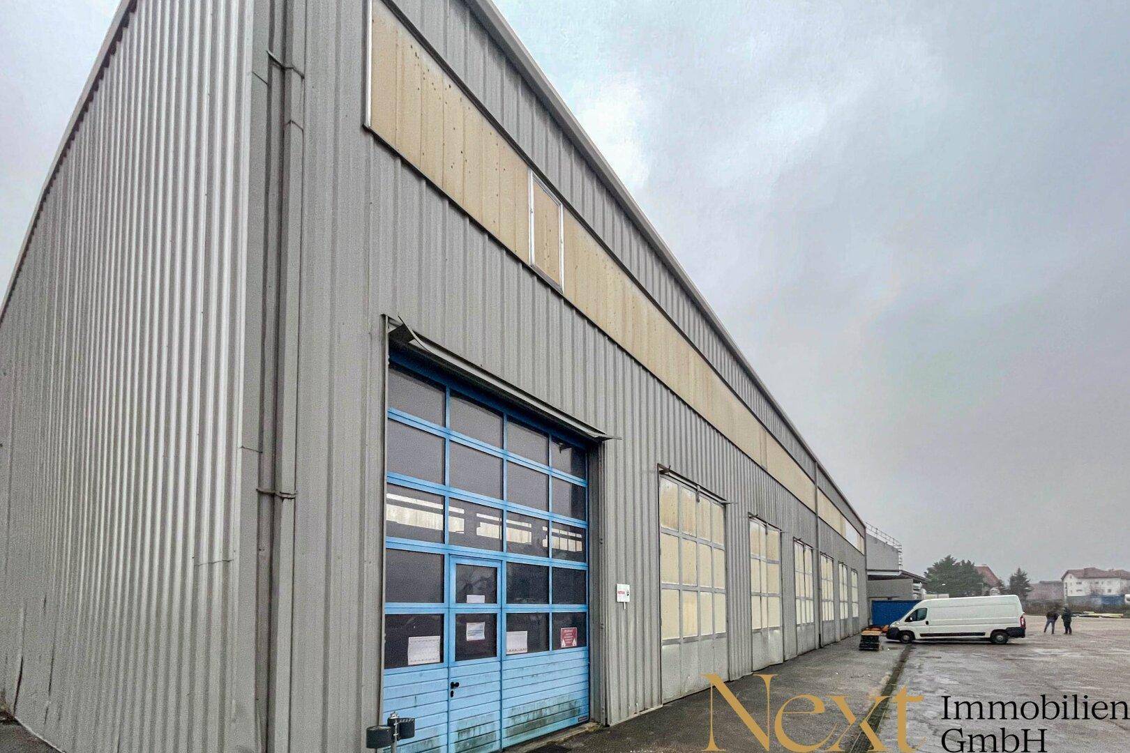 Seitenansicht einer großen Industriehalle mit Wellblechfassade und einem blauen Rolltor.