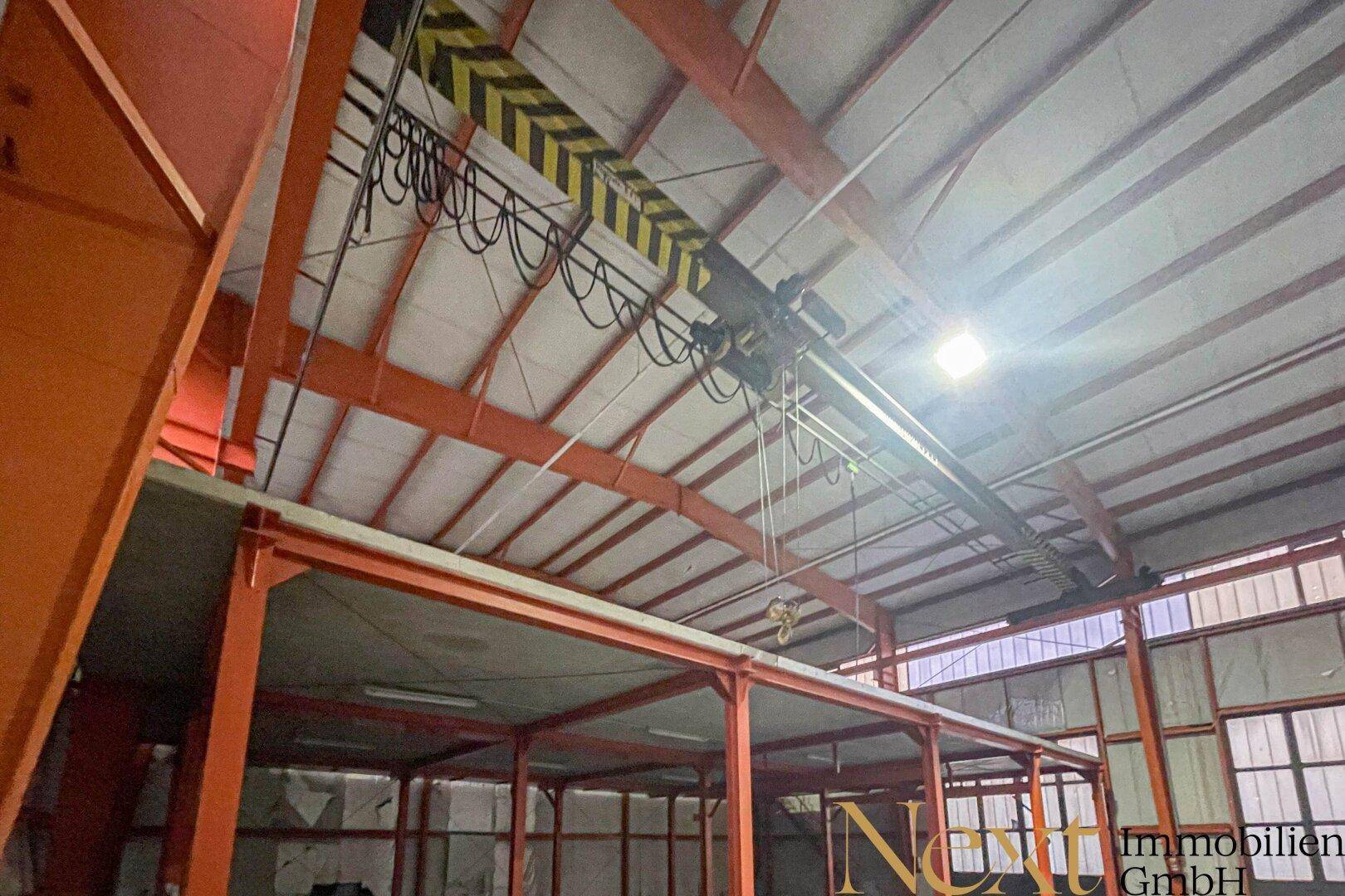 Detailansicht der hohen Decke einer Industriehalle mit orangefarbenen Stahlträgern und einem gelb-schwarzen Kran.