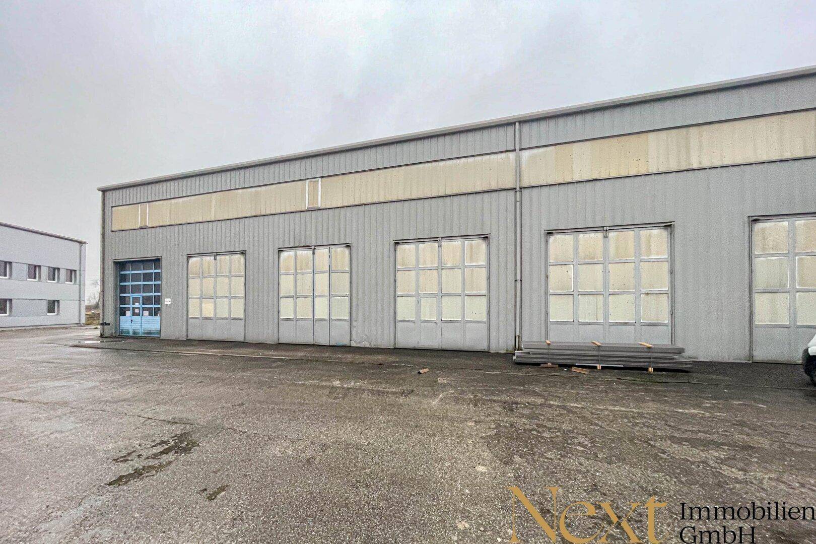 Vorderansicht einer Industriehalle mit mehreren großen Toren und einer breiten Zufahrt.