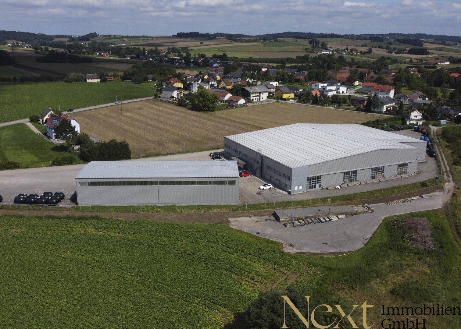 Weitläufige Luftaufnahme des Industrieareals mit zwei Hallen, umgeben von Feldern und einer ländlichen Siedlung.