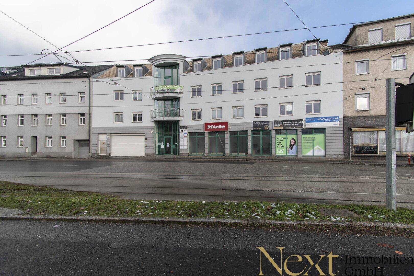 Mehrstöckiges Gebäude mit Geschäften im Erdgeschoss und Wohnungen darüber, direkt an einer belebten Straße gelegen.