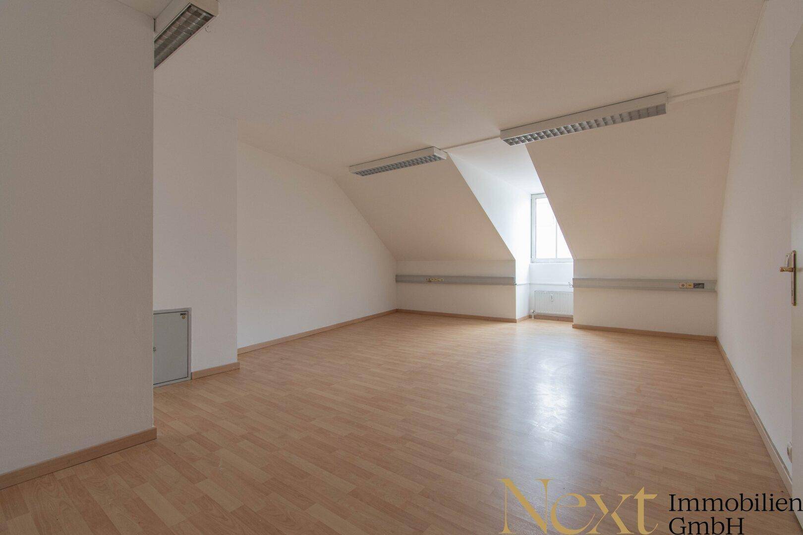 Geräumiger, leerer Dachraum mit Laminatboden und schrägen Wänden, gut beleuchtet durch Fenster.