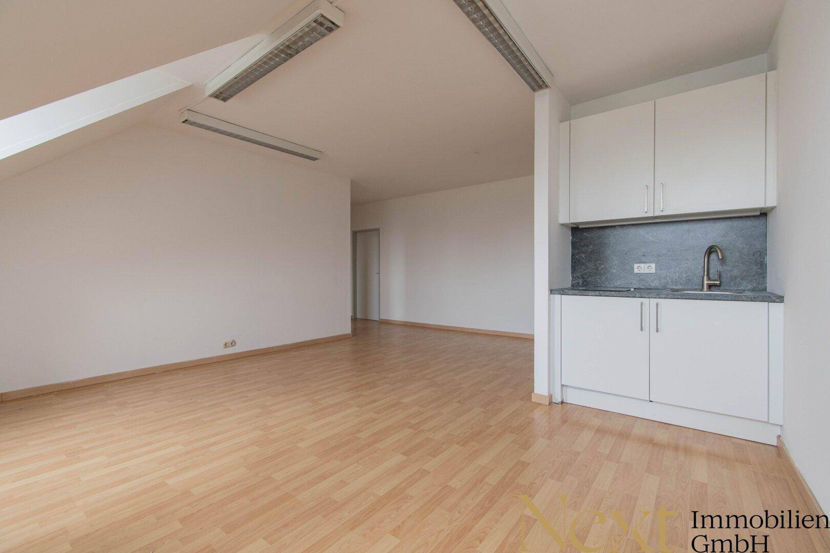 Kleine, moderne Küchenzeile mit weißen Schränken und Spüle in einem hellen Dachraum.